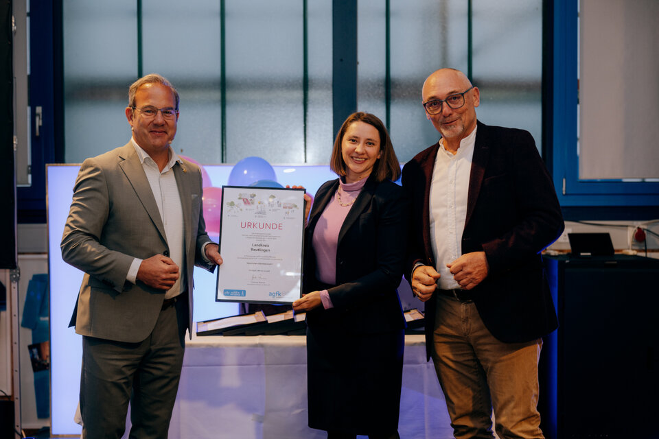 Die Erste Landesbeamtin des Landkreises Reutlingen, Greta Schirmer-Förster (m.), nimmt die Ehrung im Namen der Kreisverwaltung von Günter Riemer (r.), Vorstand der AGFK BW, und Staatssekretär Raimund Haser (l.) entgegen. 